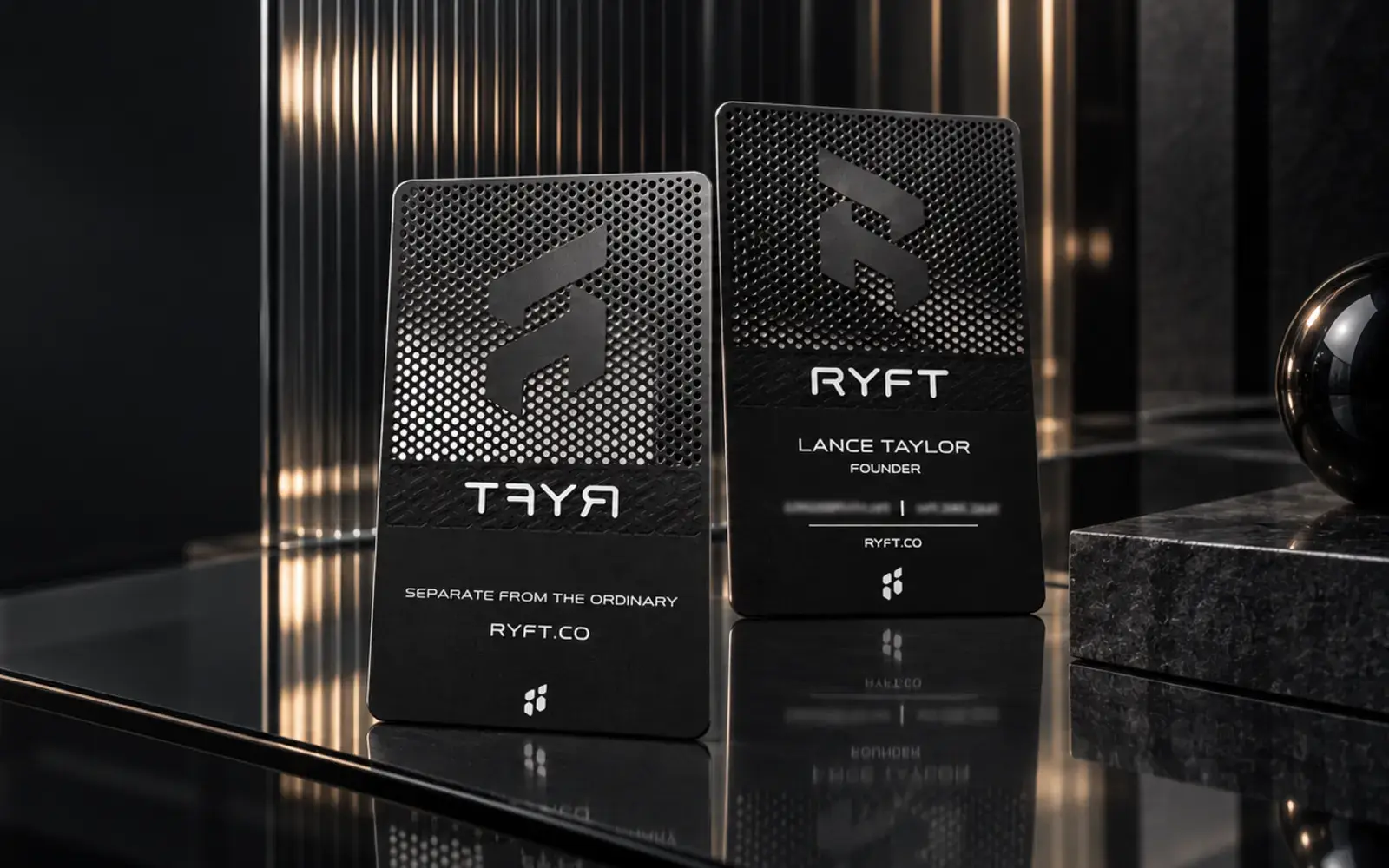 Two black metal business cards with laser-cut perforations, standing on smoked glass
