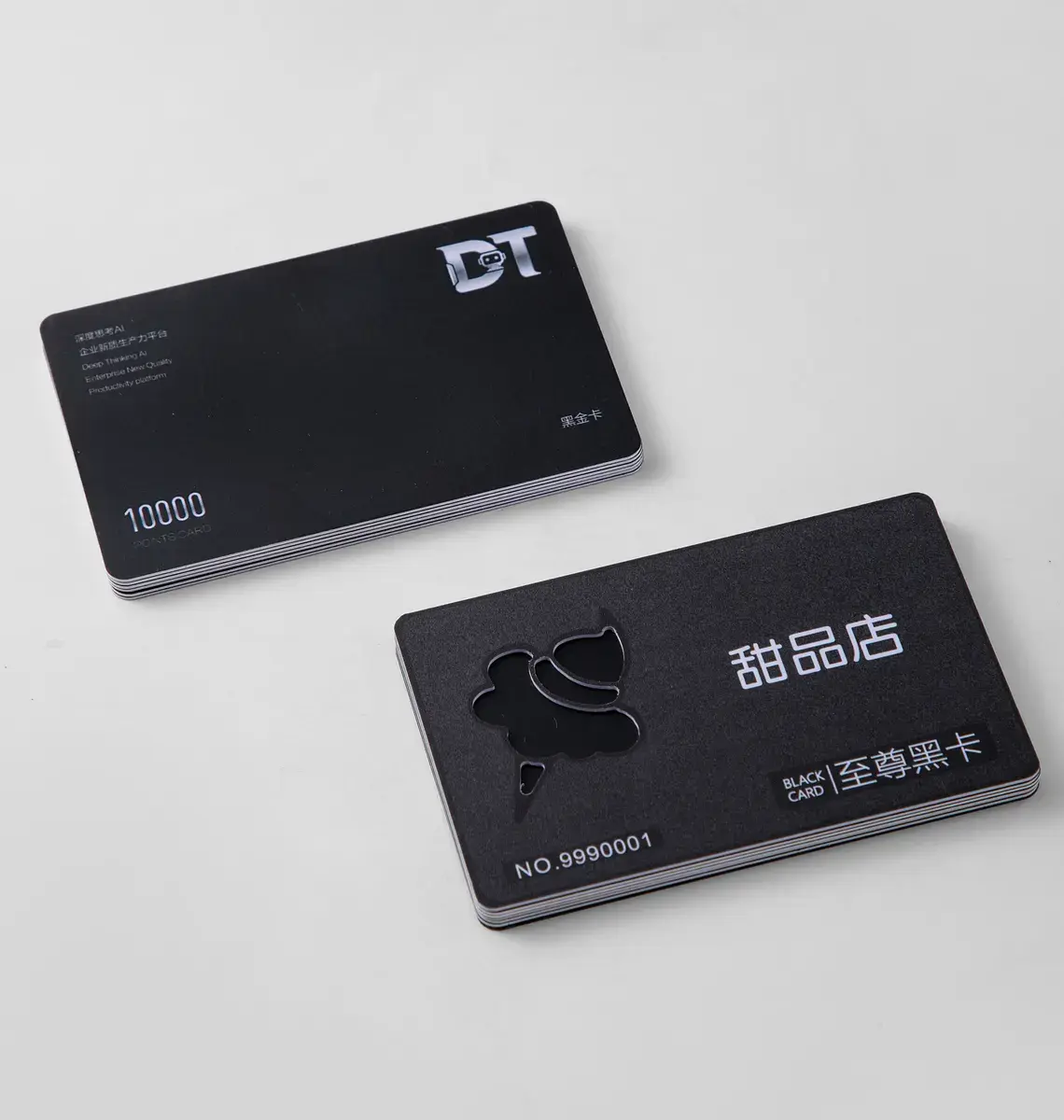 Two black PVC business cards with white print, one with a die-cut shape, on white