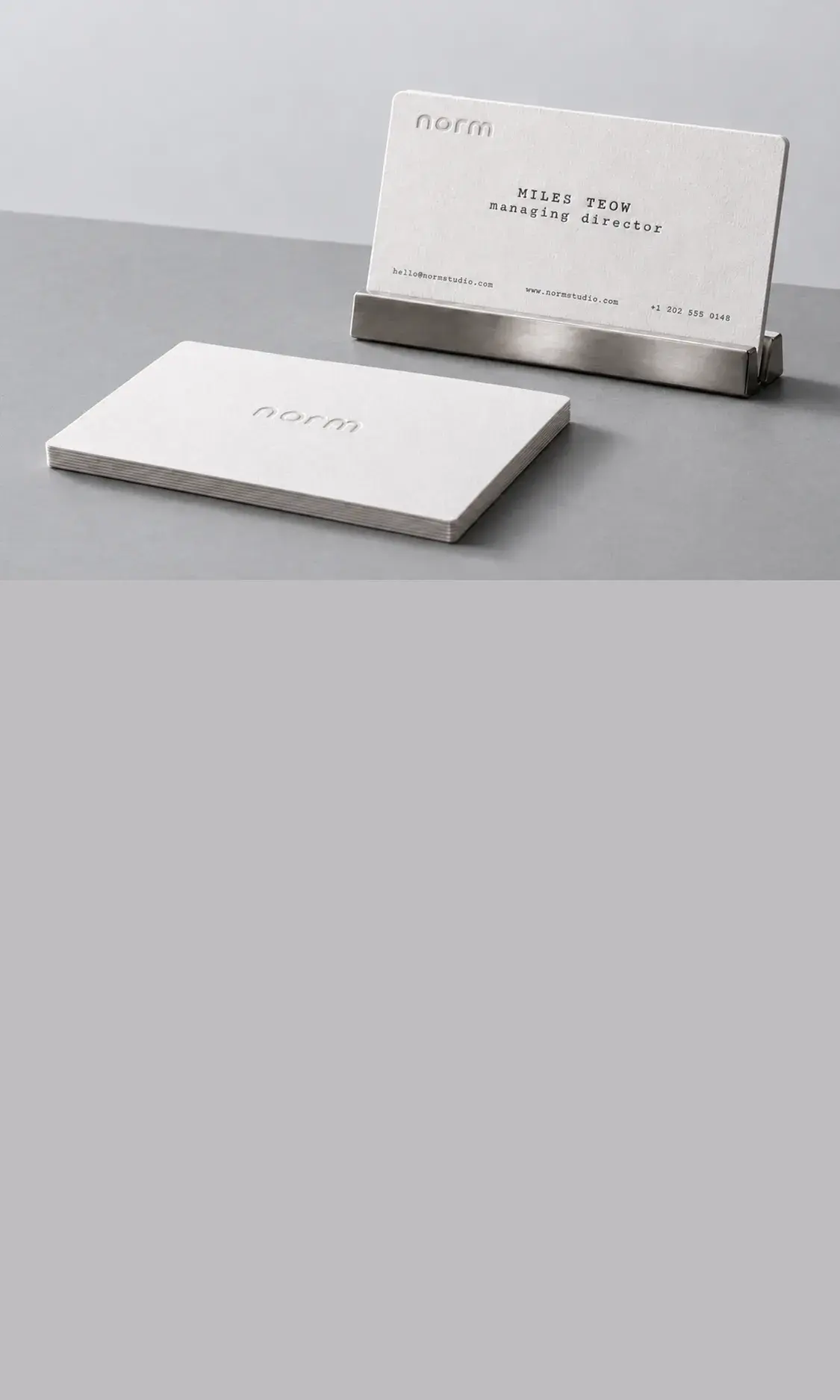 White cotton letterpress cards for norm: one in a steel stand, a stack with the logo pressed in blind