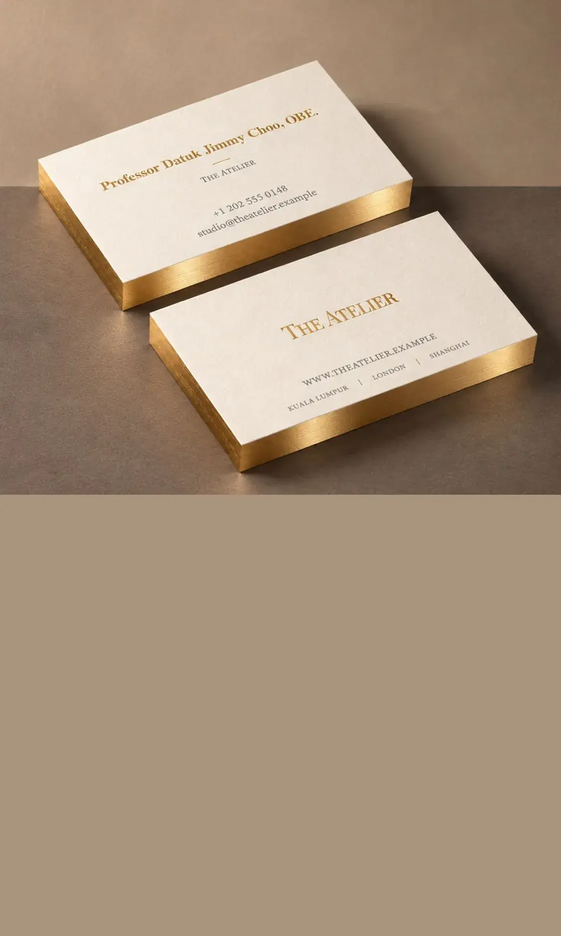 Two stacks of cream cotton cards with gold painted edges and gold type, on a warm grey table