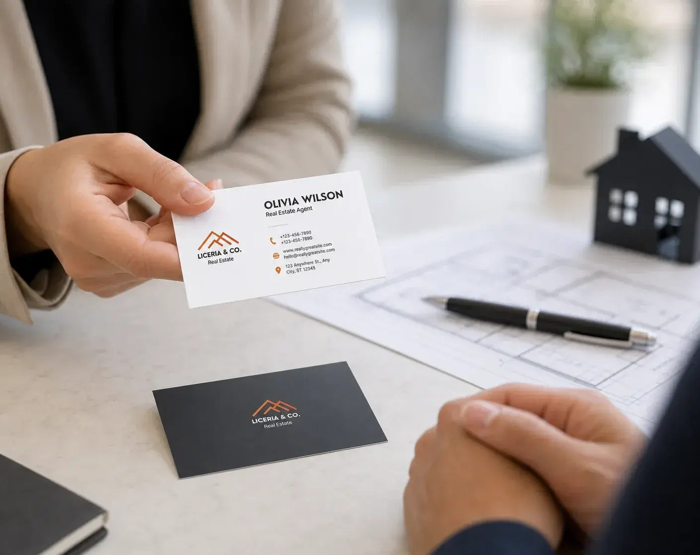 A white laminated business card handed across a desk, with a black card on the table