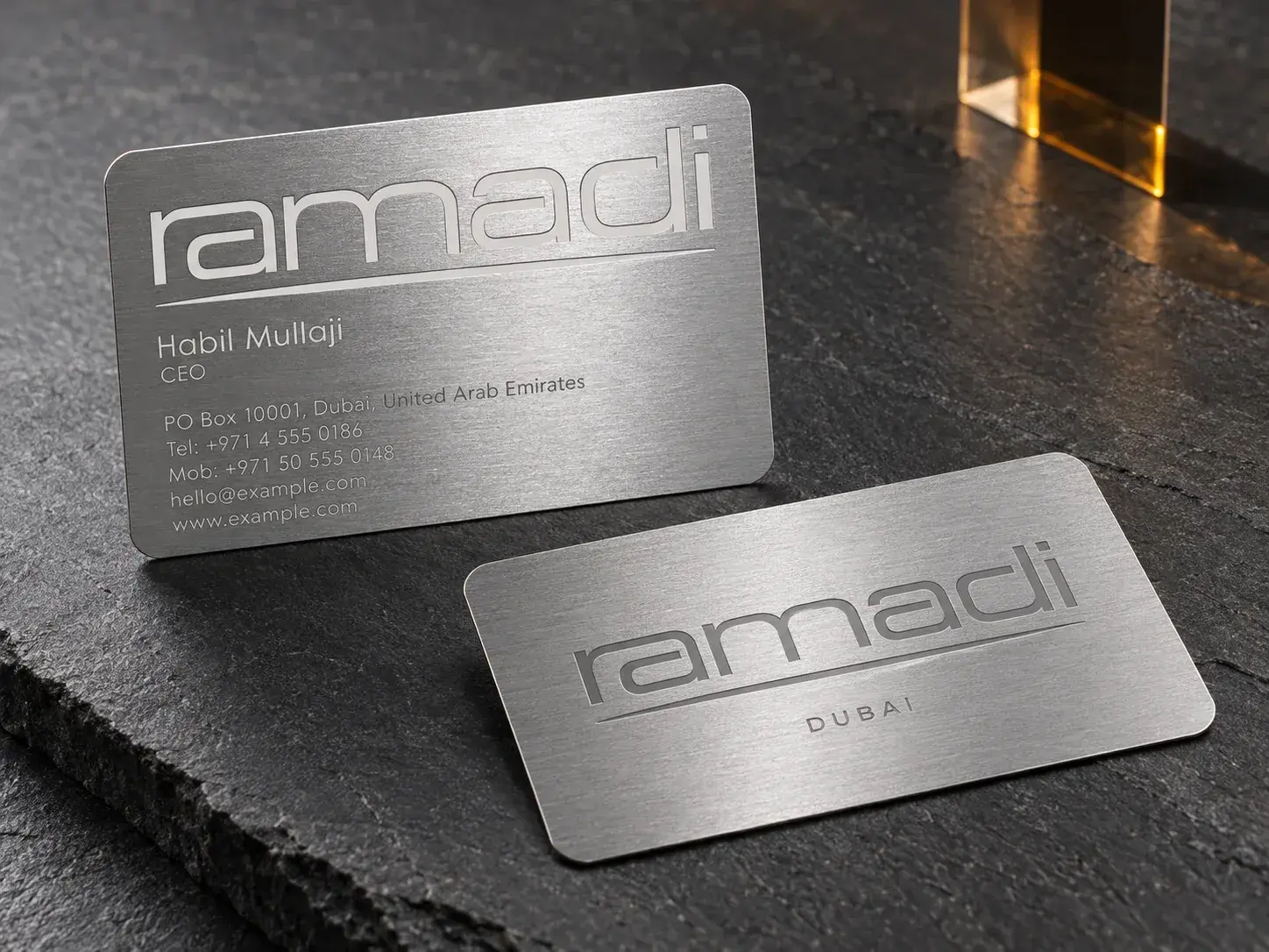 Two brushed silver metal cards with a laser-engraved wordmark on dark stone