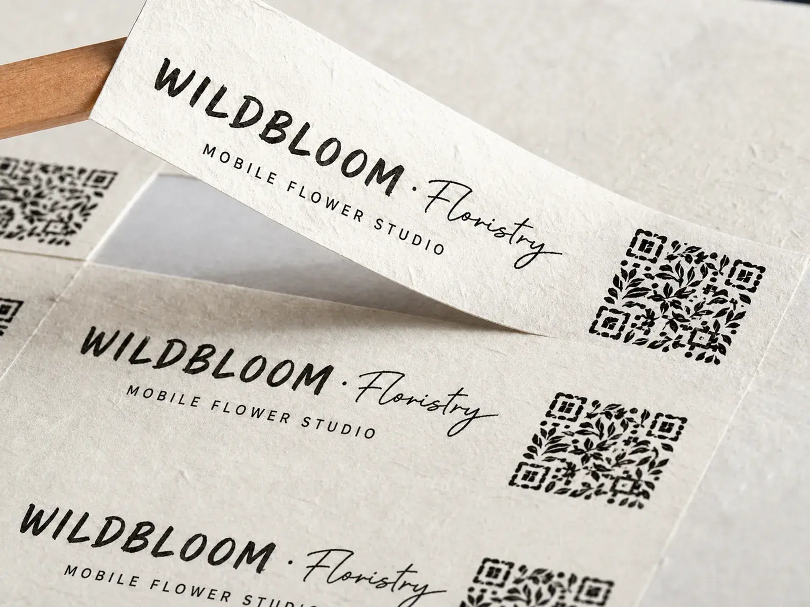 A sheet of off-white fibrous paper labels for a flower studio, one lifted with a wooden stick