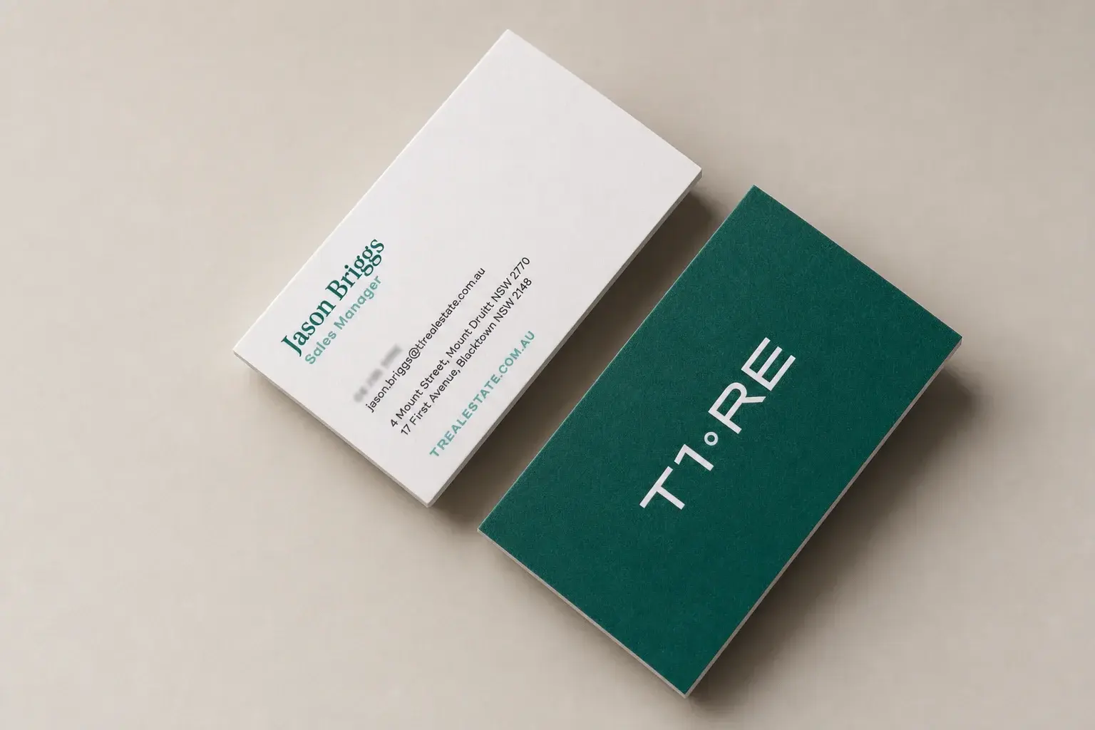 Letterpress business card: Ice White smooth fine paper with a deep teal flood front reversing a centered white wordmark split by a small ring; the white back sets a teal serif name, a light-teal bold title and website, and charcoal contact and address lines, all flush left.