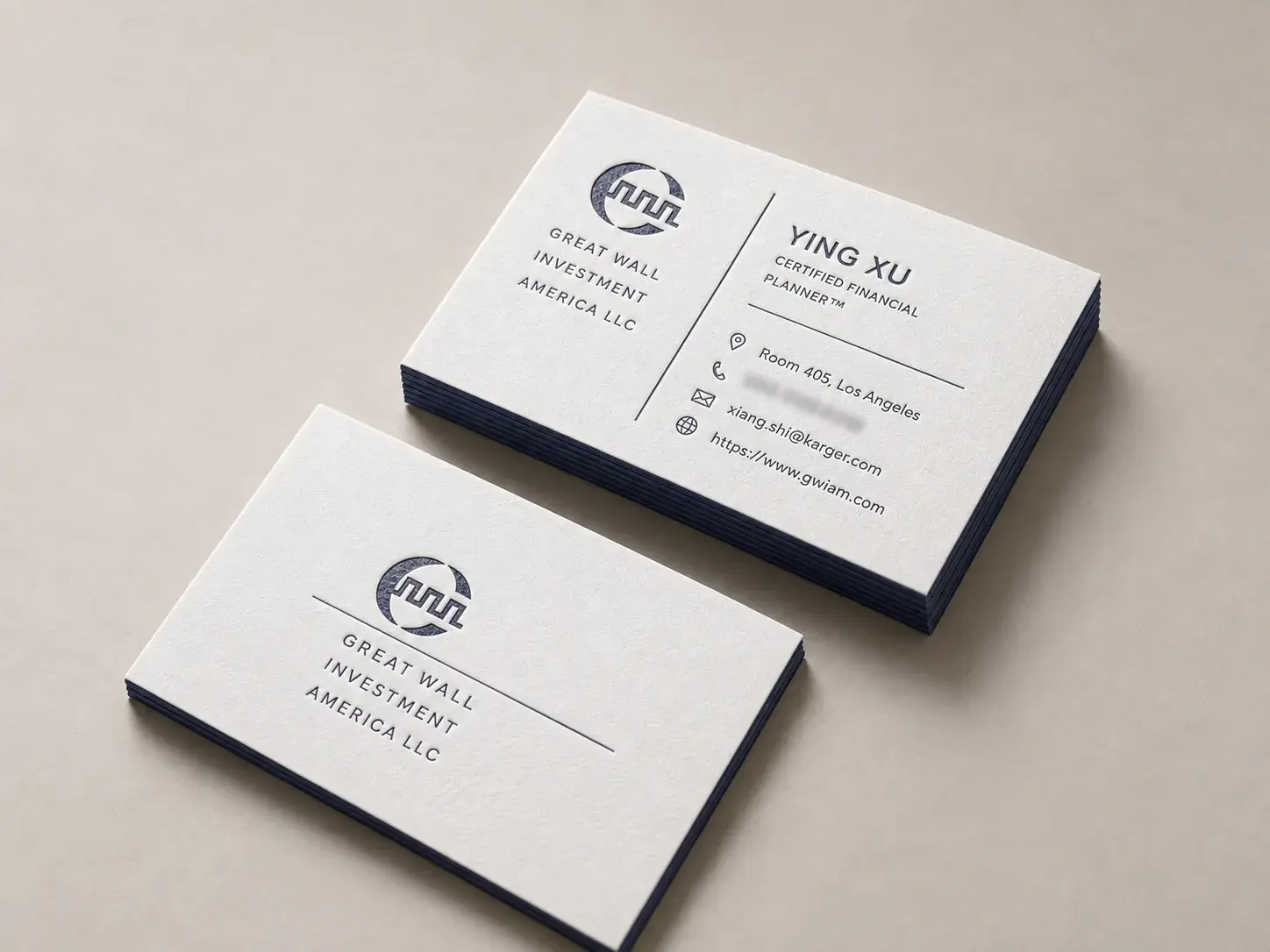 Letterpress business card: Cream-white Montericca letterpress printed in navy with navy painted edges; the front stacks an oval ring monogram over a long hairline rule and a widely tracked three-line company name, and the back splits logo and company from name, title, a short rule and four icon-led contact lines with a tall vertical hairline.