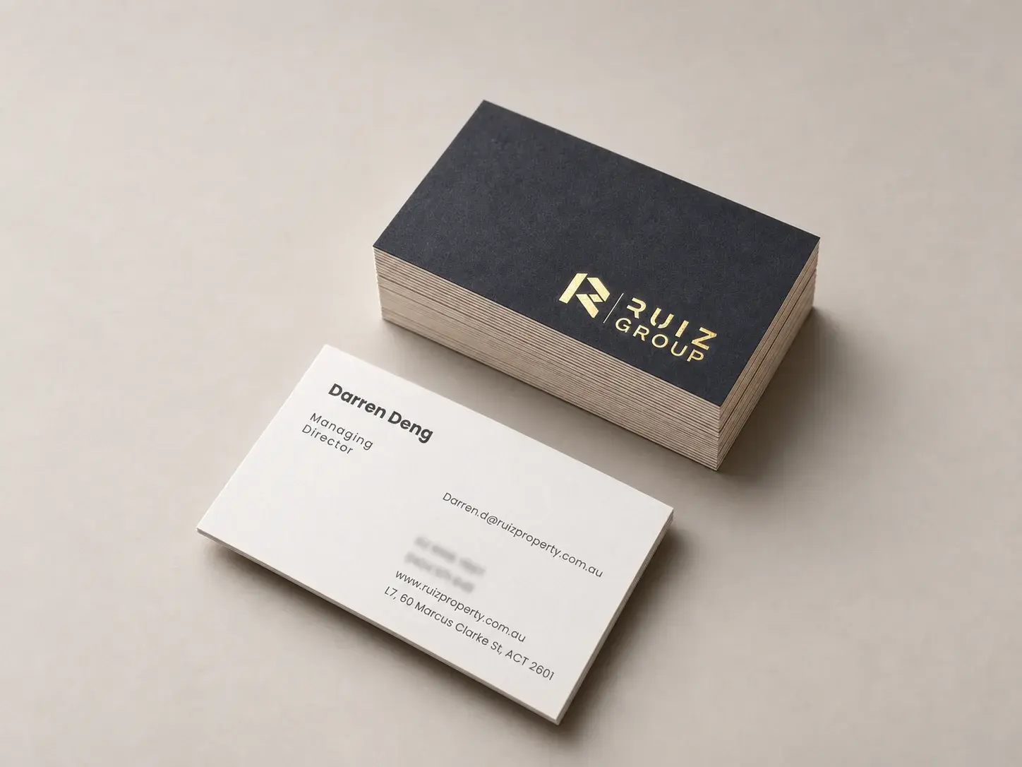 Letterpress business card: Thick 32pt smooth white fine paper with a dark slate-navy full-bleed front carrying a matte gold foil lockup bottom right (initial, thin vertical rule, two-line caps brand), and grey geometric-sans name, title and contact details on the white back.