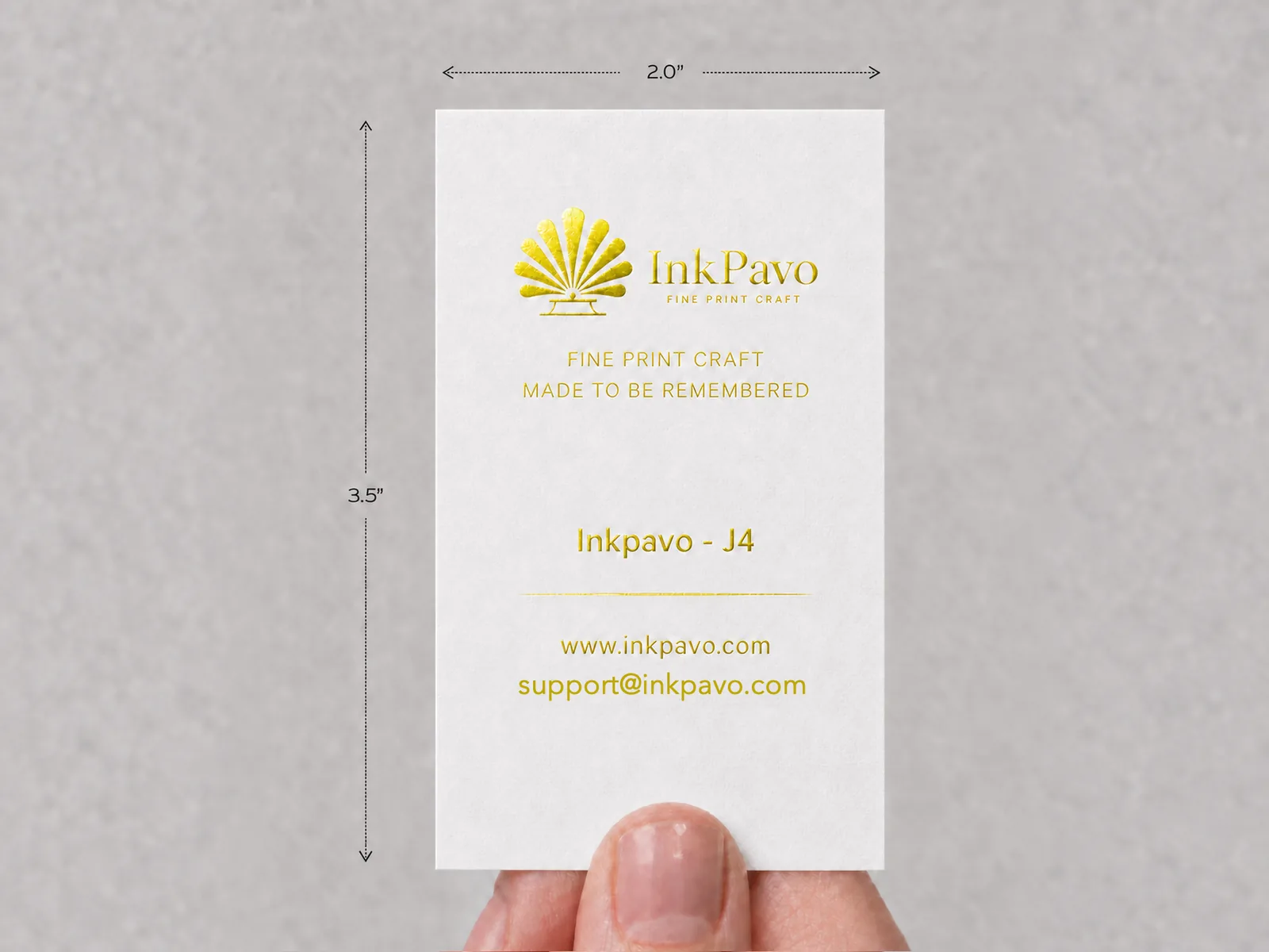 A hand holding an upright white card with the InkPavo logo hot-foil stamped in Bright Gold