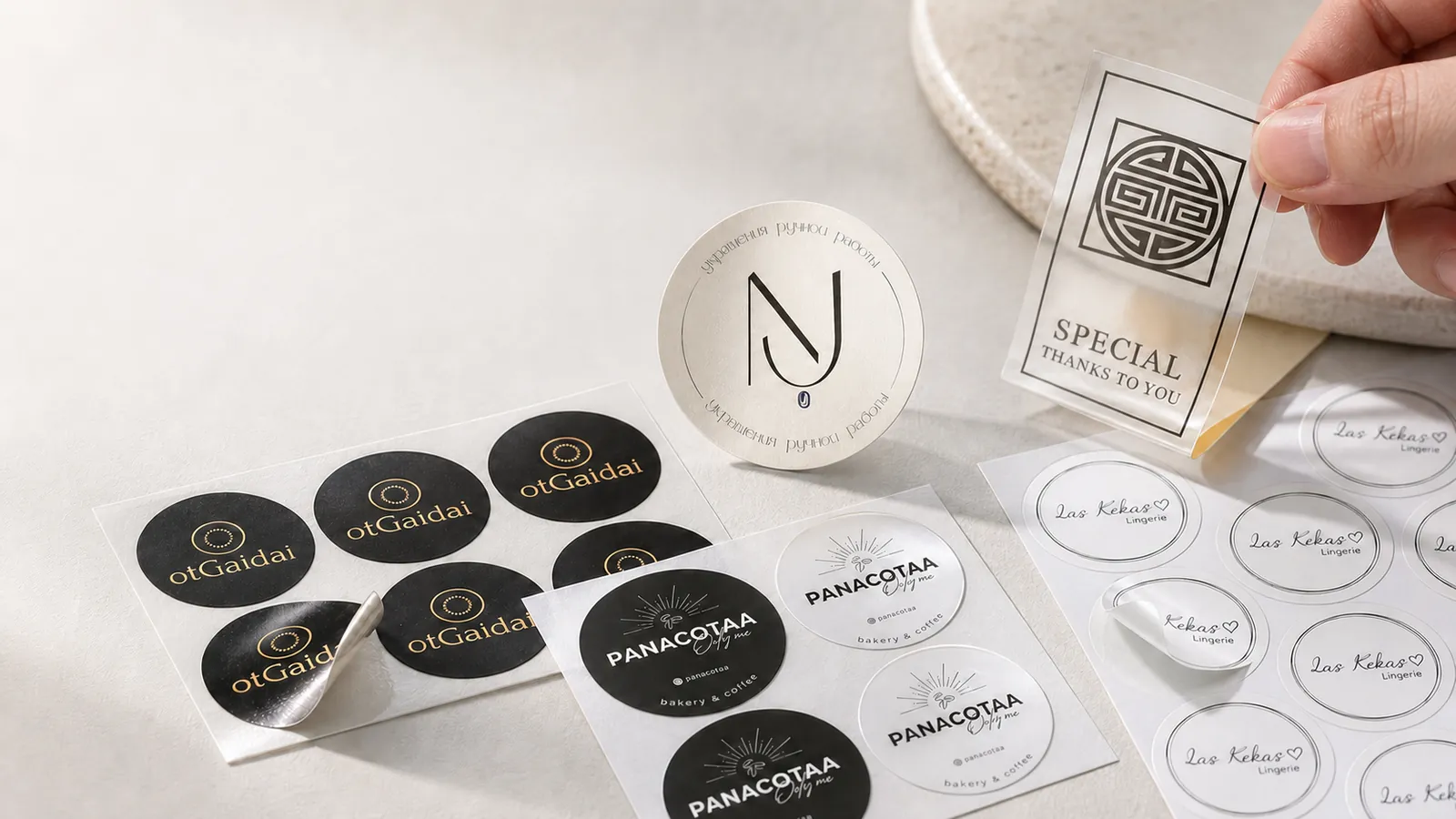 Three sheets of round paper and clear stickers, some half peeled, and a hand peeling a clear thank-you label